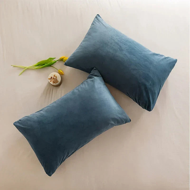 Two blue velour cushion covers styled elegantly on a neutral bedsheet with yellow floral accents.