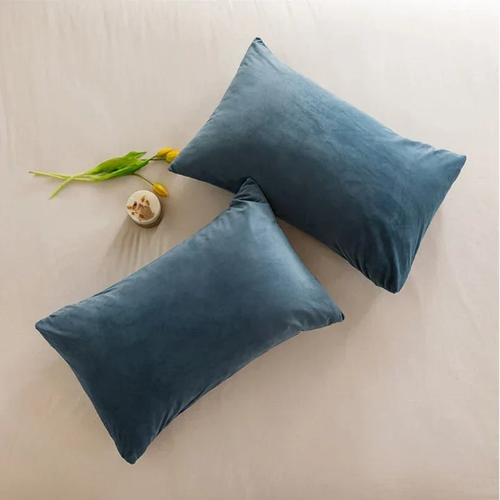 Two blue velour cushion covers styled elegantly on a neutral bedsheet with yellow floral accents.