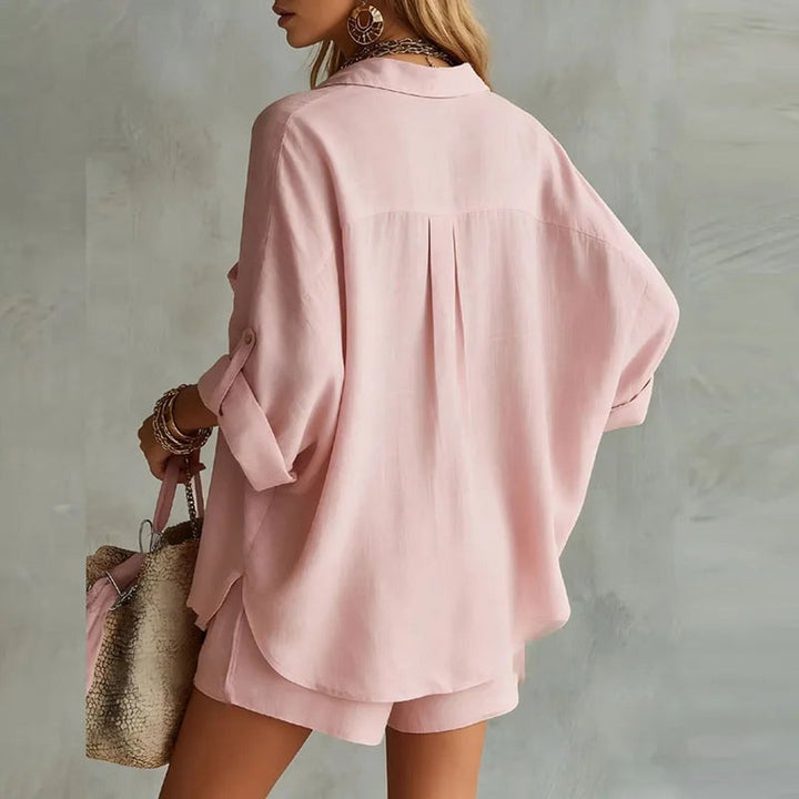 Back view of a woman wearing a pink long-sleeve top and shorts set against a neutral wall