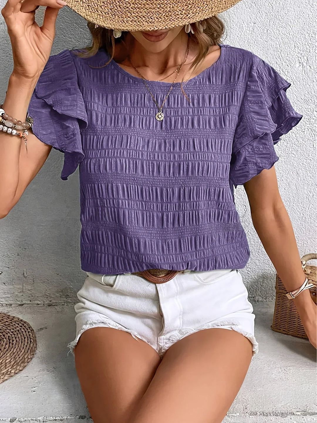 Woman wearing a purple short ruffle sleeve blouse paired with white denim shorts