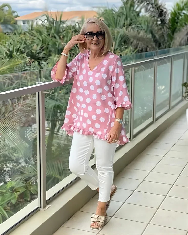 Woman wearing pink polka dot V-neck tee with white trousers and sandals outdoors