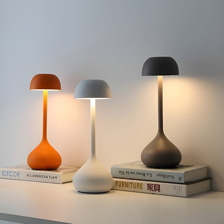 Three wireless mushroom table lamps in orange, matte white, and matte gray displayed on books
