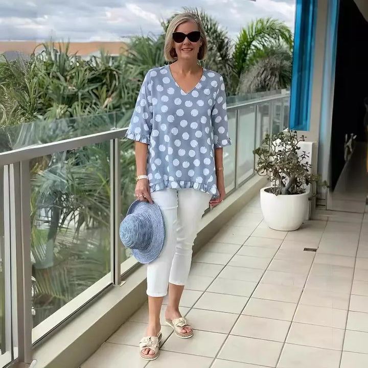 Woman wearing blue polka dot V-neck tee holding a blue hat on a balcony