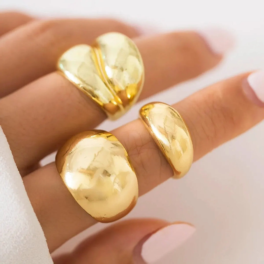 Close-up of three glossy gold-tone statement rings worn on fingers