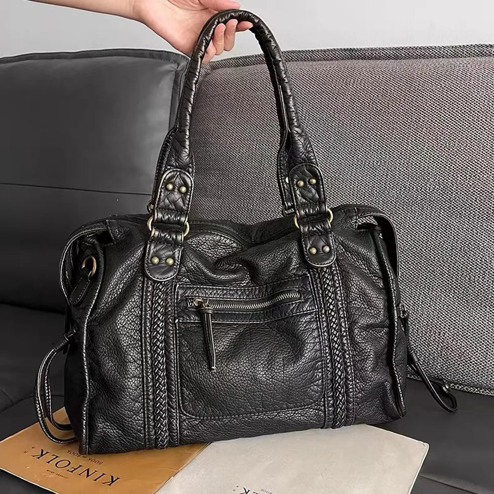 Women's black handbag held up showcasing textured design and handles