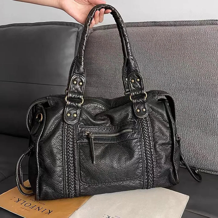 Women's black handbag held up showcasing textured design and handles