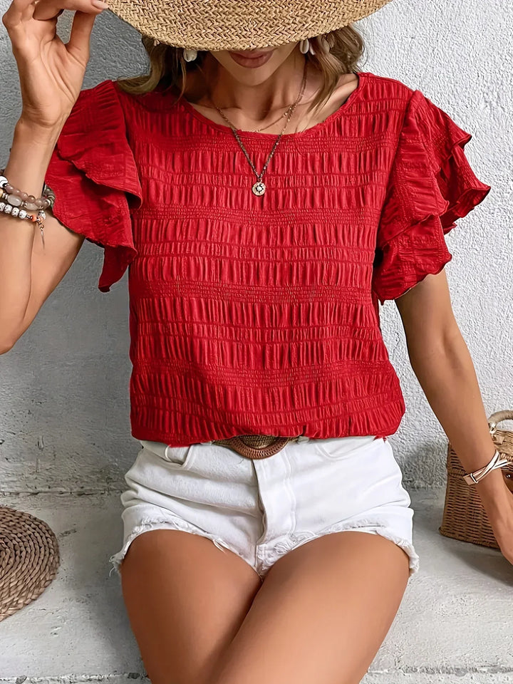 Woman wearing a red short ruffle sleeve blouse paired with white denim shorts