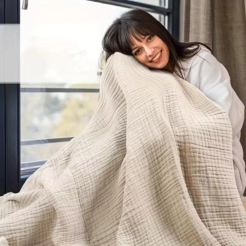 Smiling woman wrapped comfortably in a cozy muslin throw blanket near a window