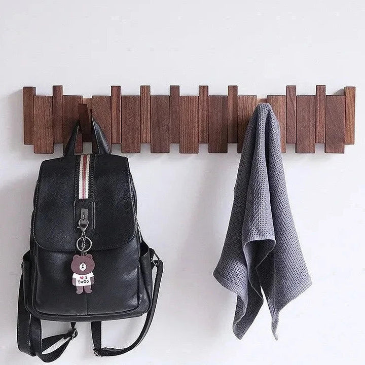 Wooden wall mounted coat rack holding a black backpack and a towel