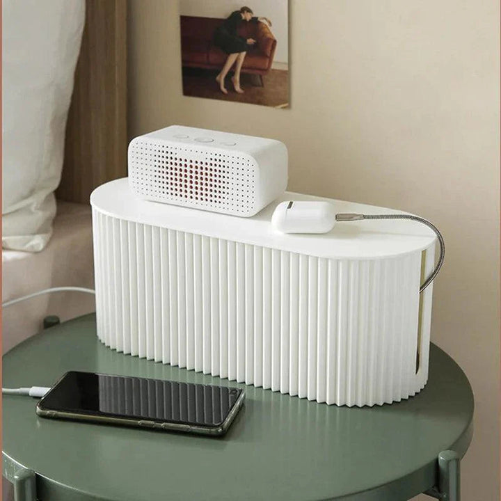 White cable organiser box on a bedside table holding a small speaker and phone