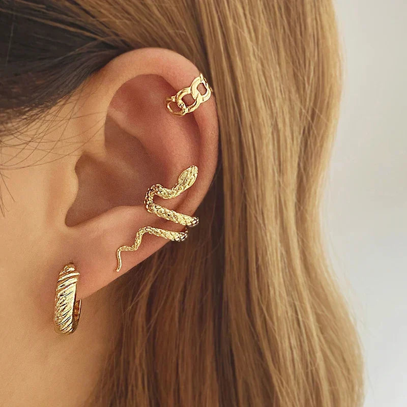 Gold tone snake ear cuff worn on model's ear cartilage with other jewelry