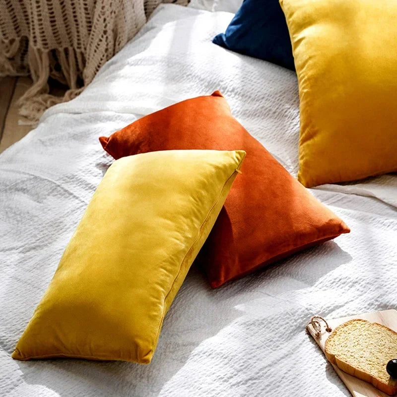 Assorted colorful velour cushion covers in yellow and orange arranged on a textured white bedspread.
