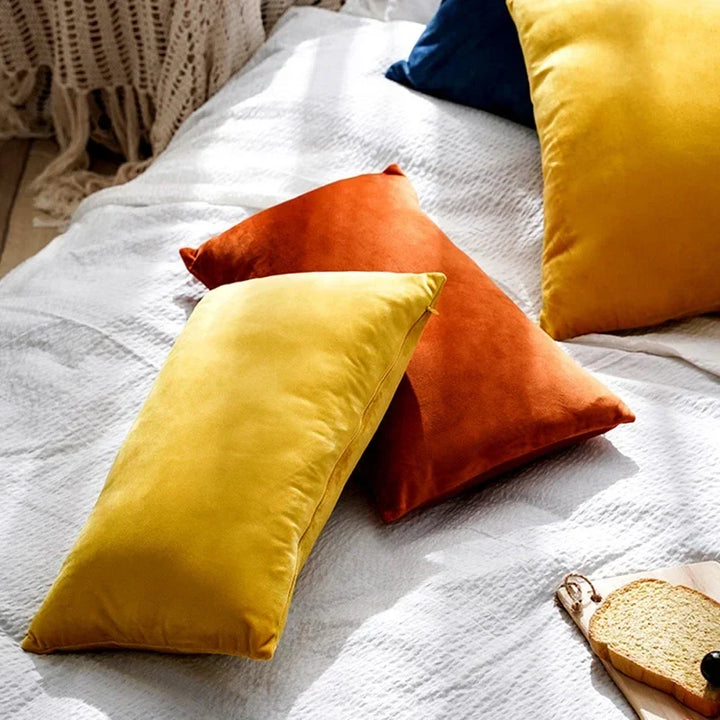 Assorted colorful velour cushion covers in yellow and orange arranged on a textured white bedspread.