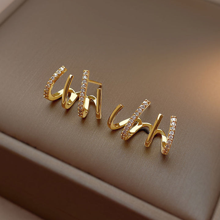 Pair of gold claw hoop earrings resting on a neutral display surface