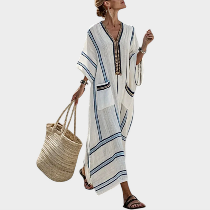 Woman wearing a white maxi dress with blue striped detailing and carrying a woven beach bag