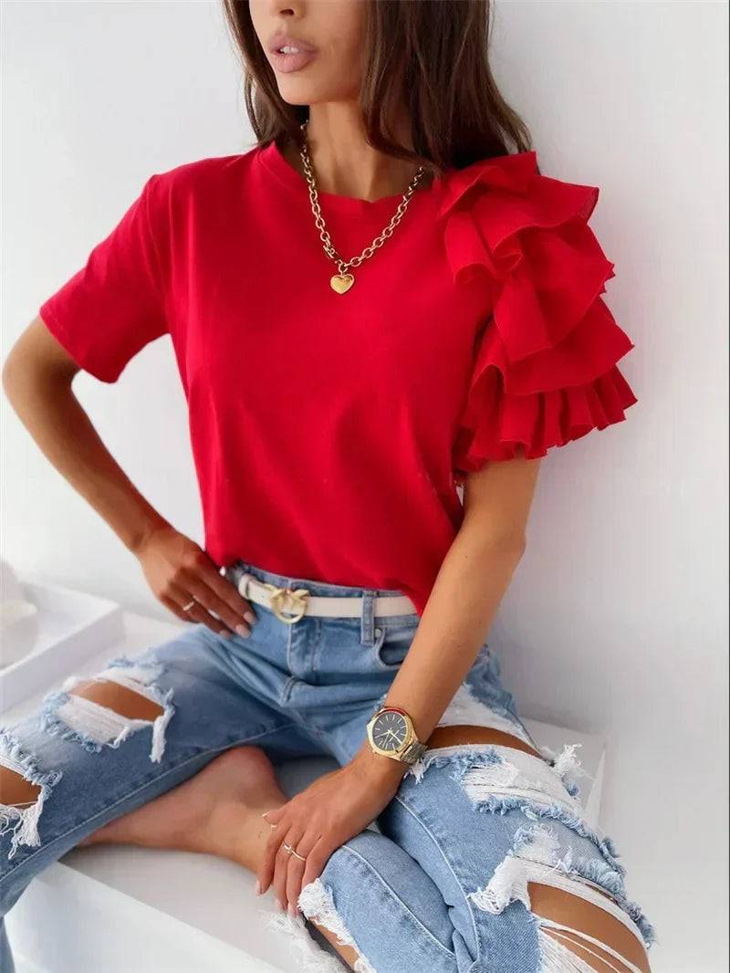 Woman wearing a bright red chic top with bold layered ruffle sleeves, paired with distressed denim jeans.