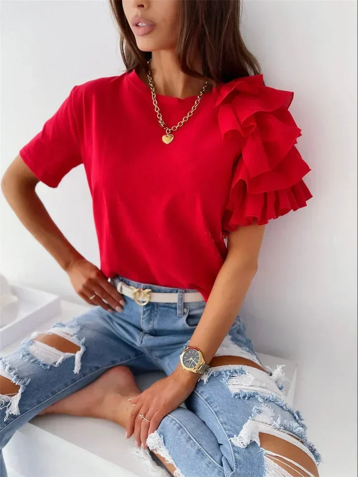 Woman wearing a bright red chic top with bold layered ruffle sleeves, paired with distressed denim jeans.