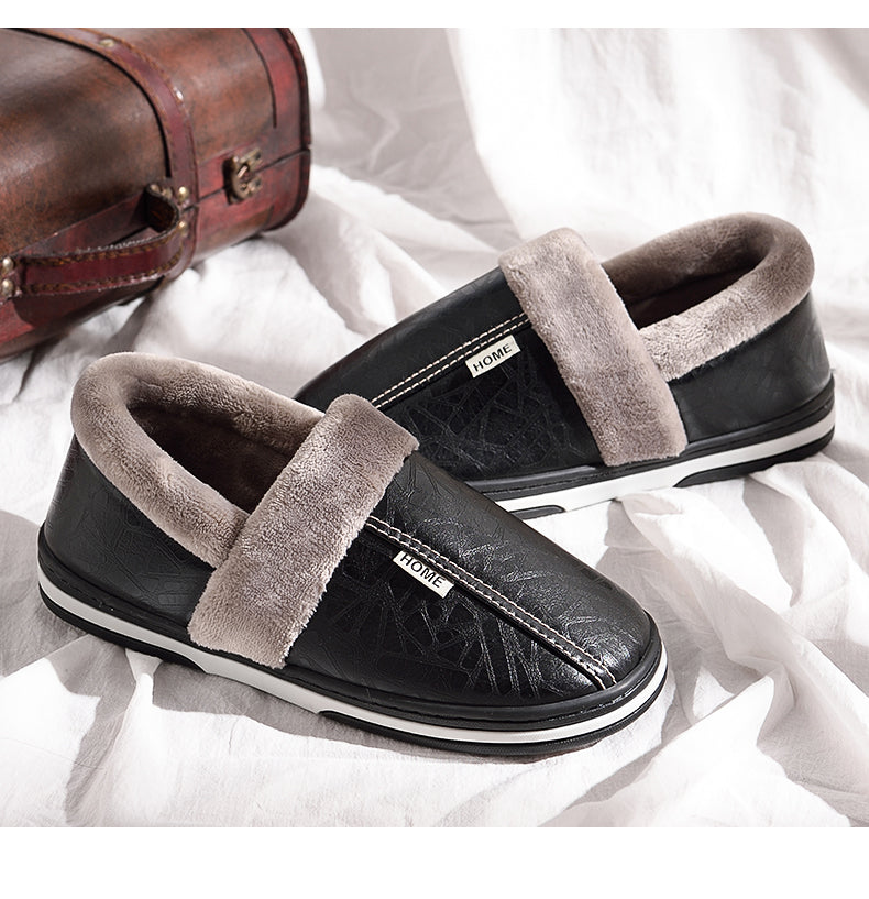 Pair of black plush lined indoor slippers resting on a soft white sheet