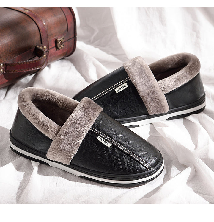 Pair of black plush lined indoor slippers resting on a soft white sheet