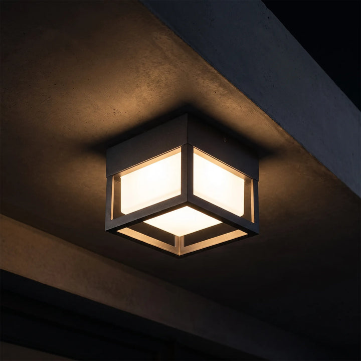 Modern black smart wall light mounted on an exterior concrete ceiling casting warm illumination.