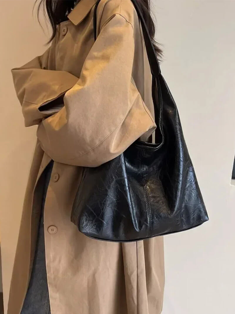 Woman wearing a black minimalist shoulder bag outdoors with beige coat