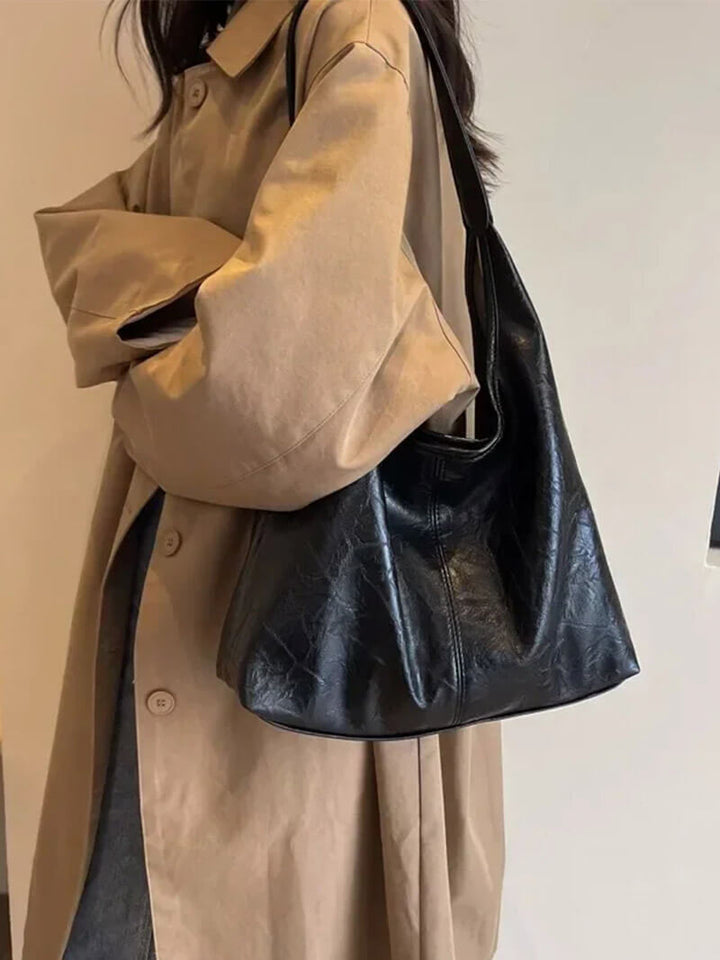 Woman wearing a black minimalist shoulder bag outdoors with beige coat