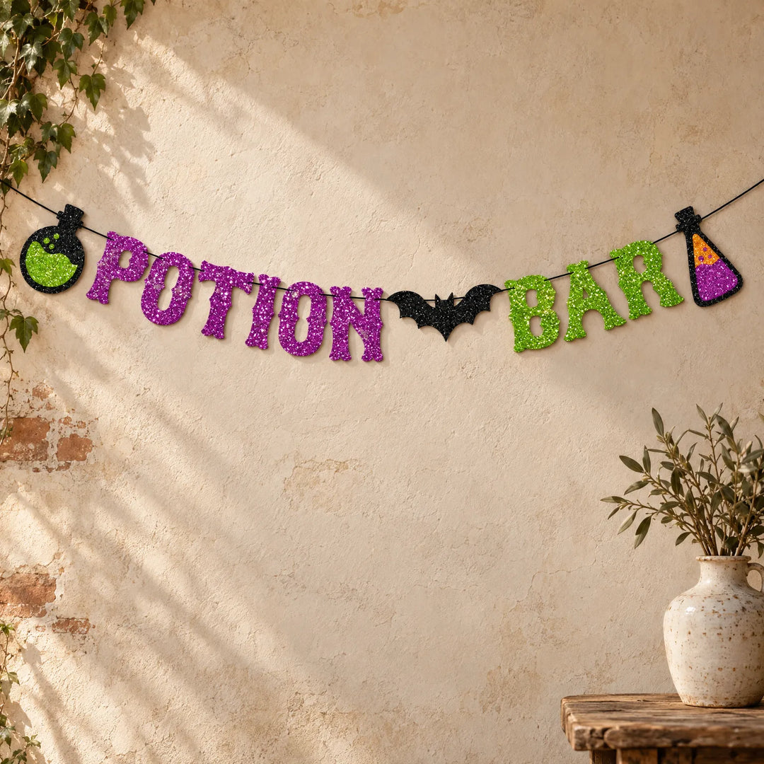 Spooky Halloween glitter potion bar banner hanging against a neutral wall with a plant vase