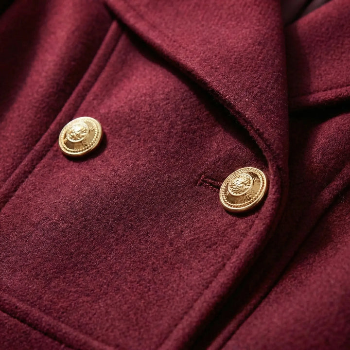 Close-up detail of the gold metallic buttons and textured fabric on the wine red short coat.