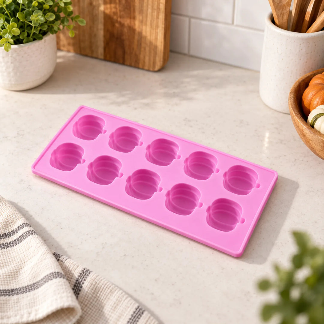 Pink pumpkin silicone chocolate mould resting on a kitchen counter next to autumn decor