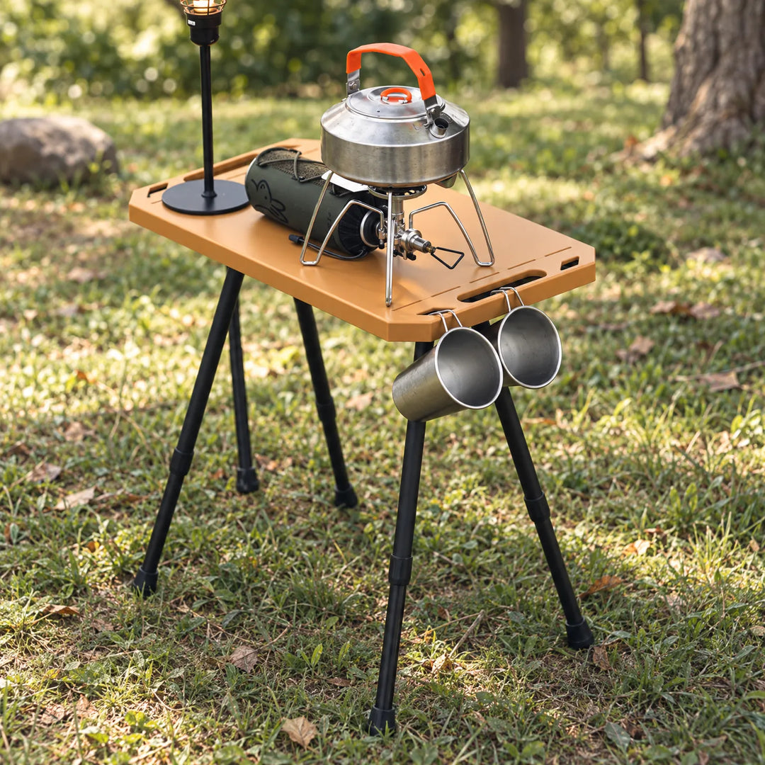 Outdoor camping table set up in a forest with cooking gear on top