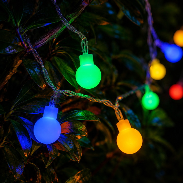 Close-up of glowing multicolored LED fairy bulbs hanging among green foliage