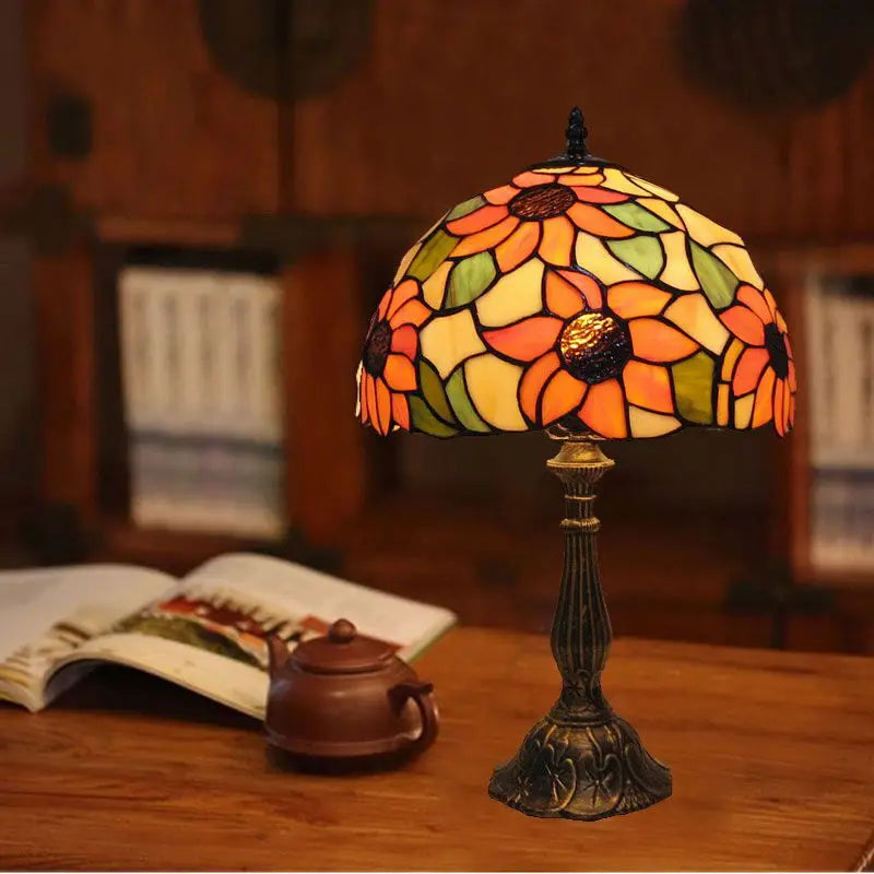 Tiffany stained glass table lamp with floral shade glowing on a wooden desk
