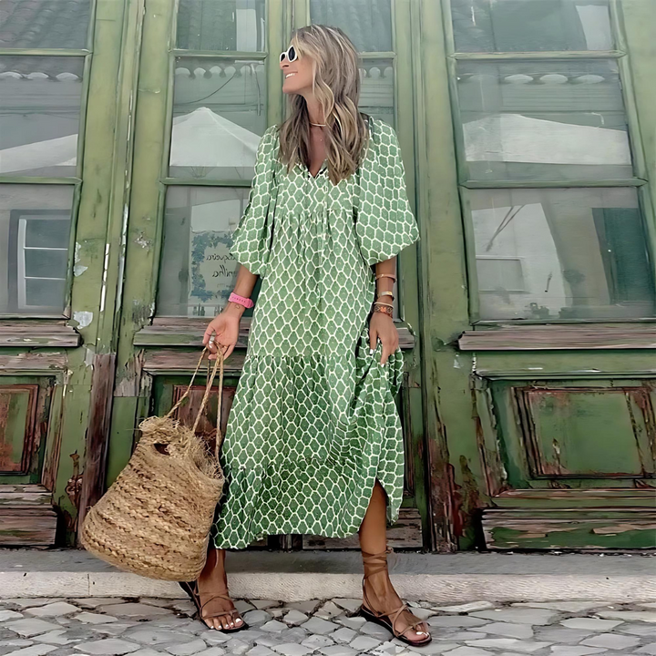 Full length view of a woman in a green geometric print dress holding a straw bag