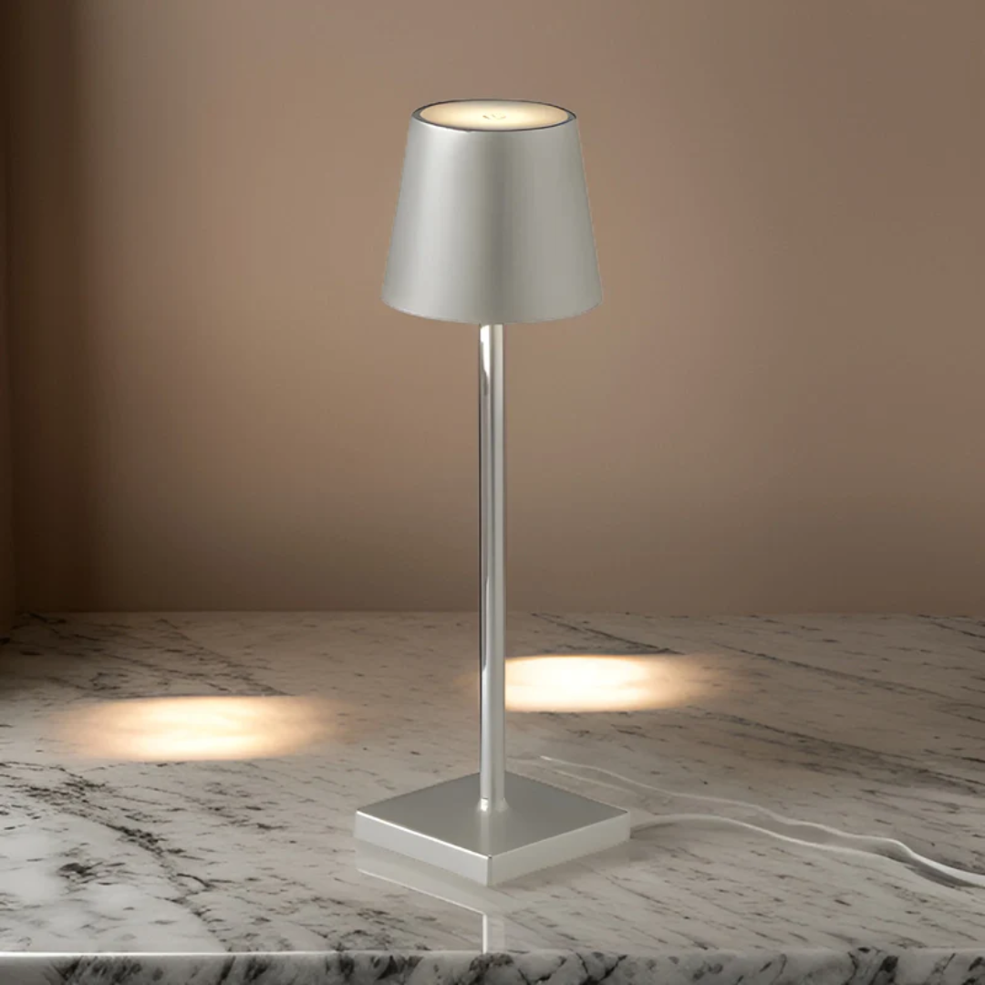 Single silver wireless rechargeable table lamp illuminated against a warm neutral wall