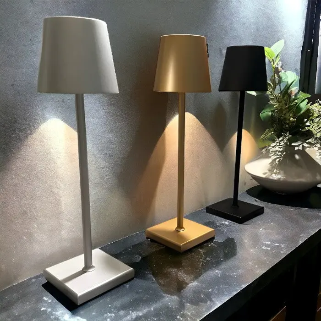 Three wireless rechargeable table lamps in white, gold, and black displayed on a dark surface