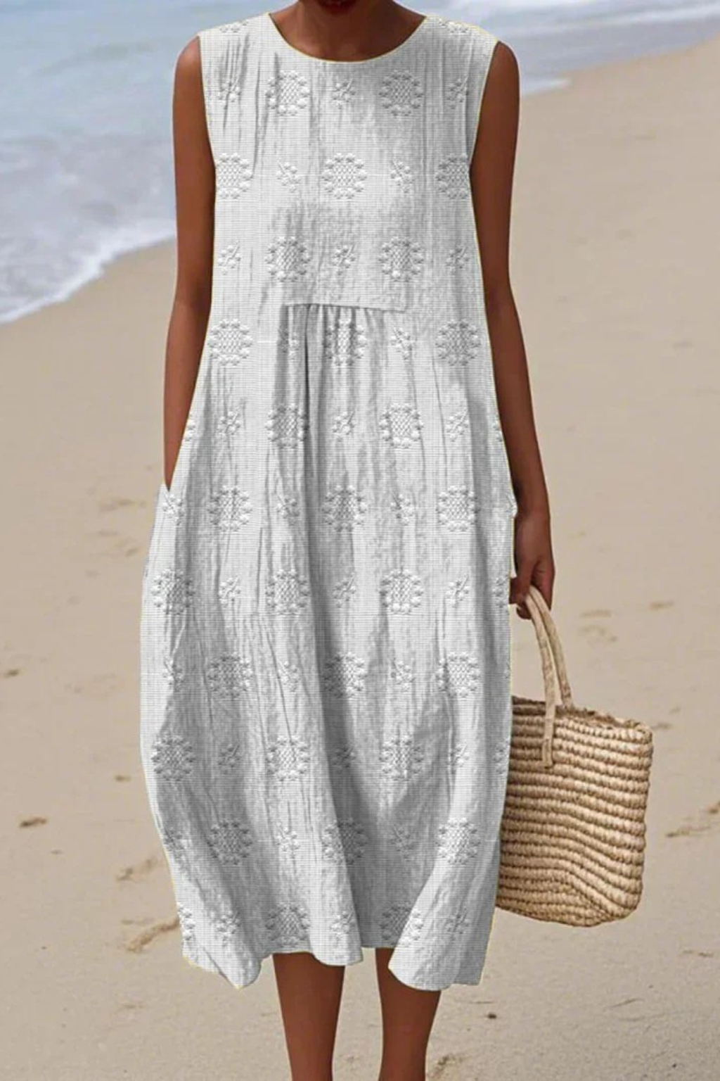 Woman wearing white embroidered sleeveless midi dress holding straw bag