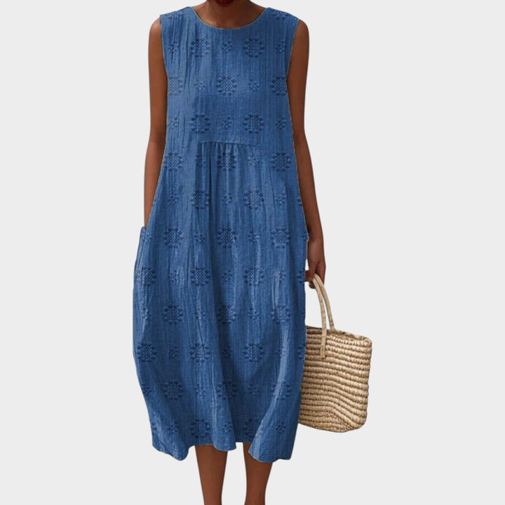 Woman wearing a blue sleeveless summer midi dress with textured floral patterns and side pockets