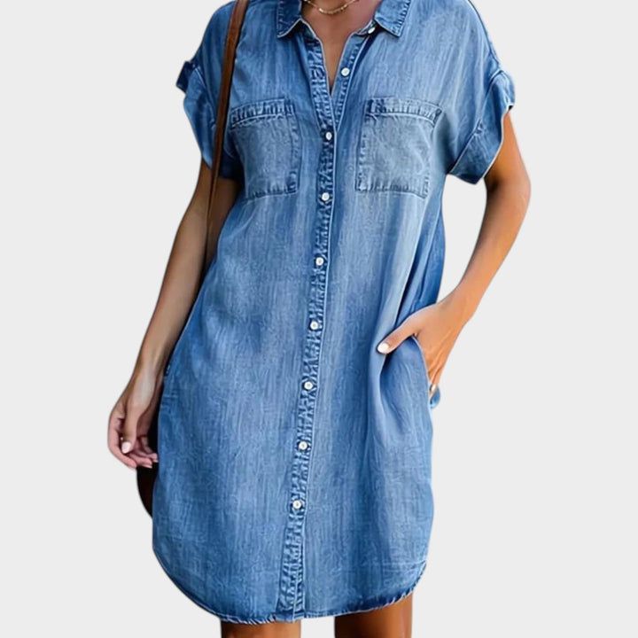Woman wearing light blue mini denim shirt dress with buttons and pockets