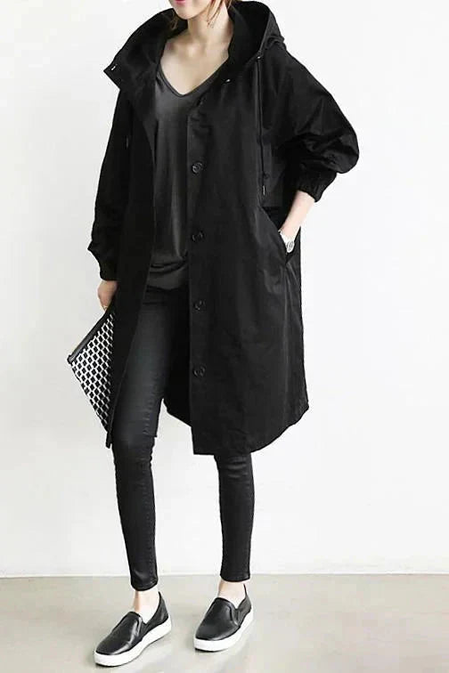 Woman wearing a black hooded raincoat with dark trousers and slip-on shoes