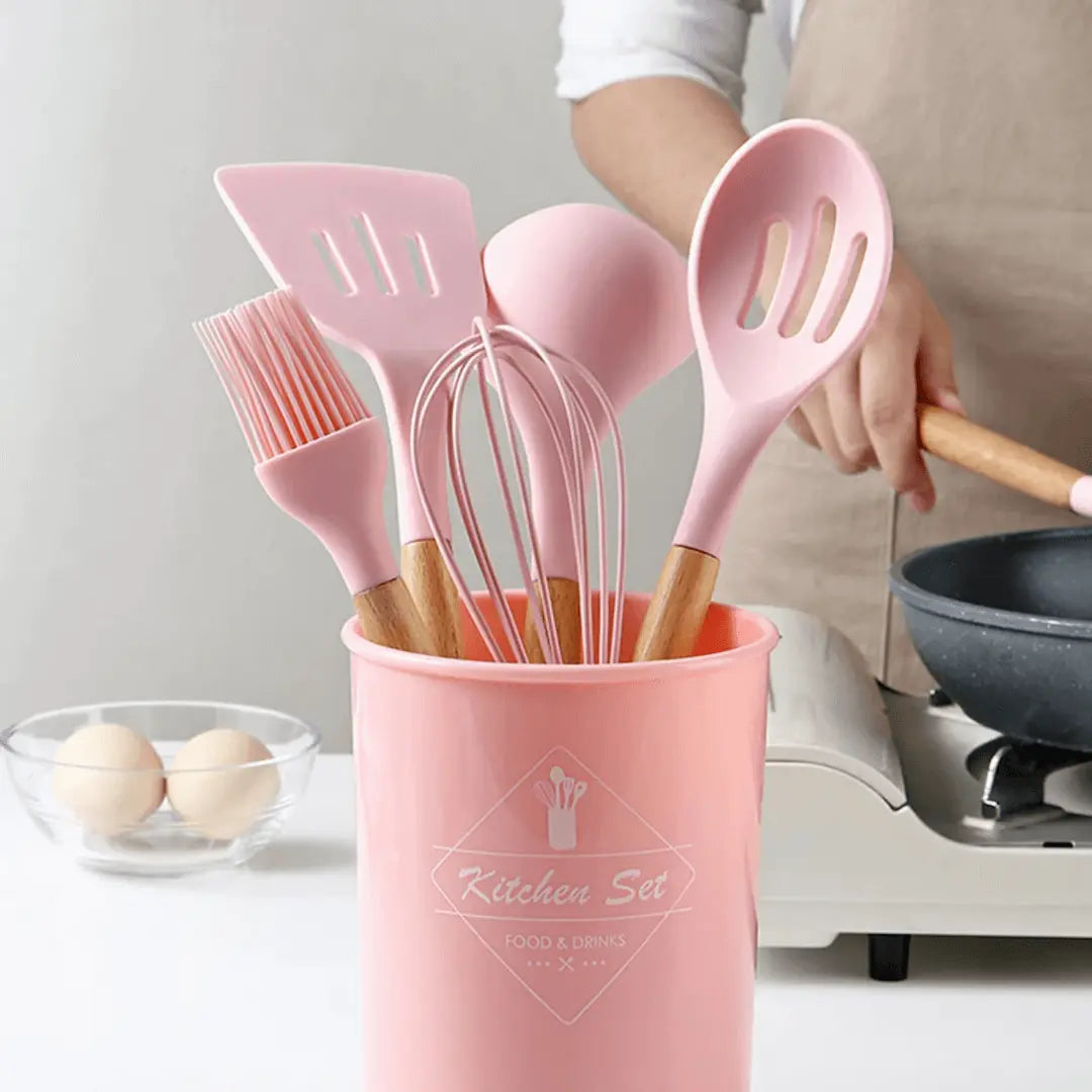Pink silicone kitchen utensil set displayed in a matching holder with a whisk and spatulas