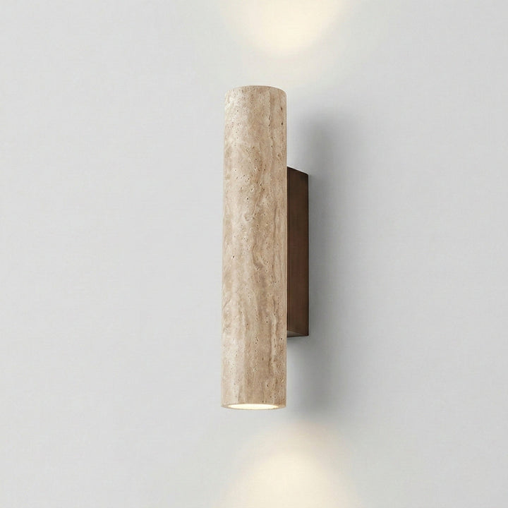 Natural travertine vertical cylinder wall lamp lit on a white wall