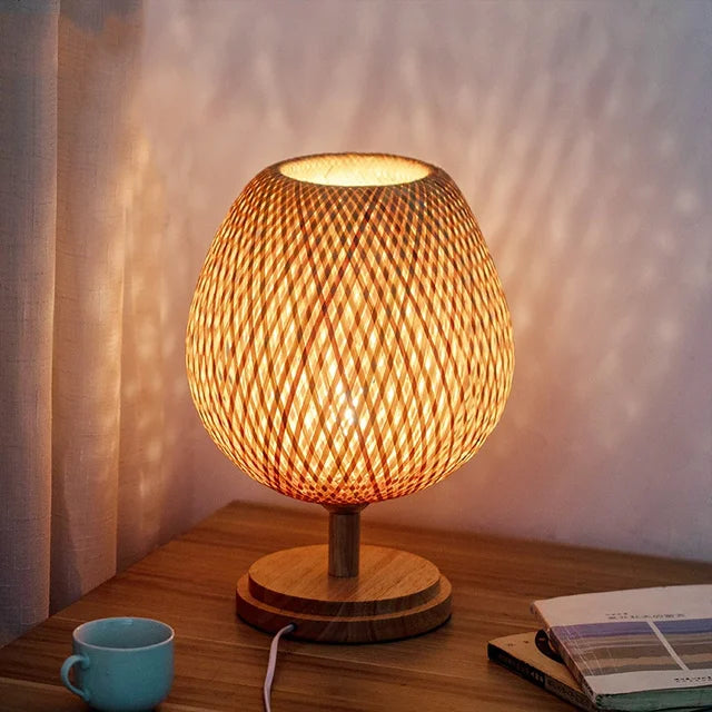 Illuminated woven bamboo table lamp with a wooden base casting patterns on a wall