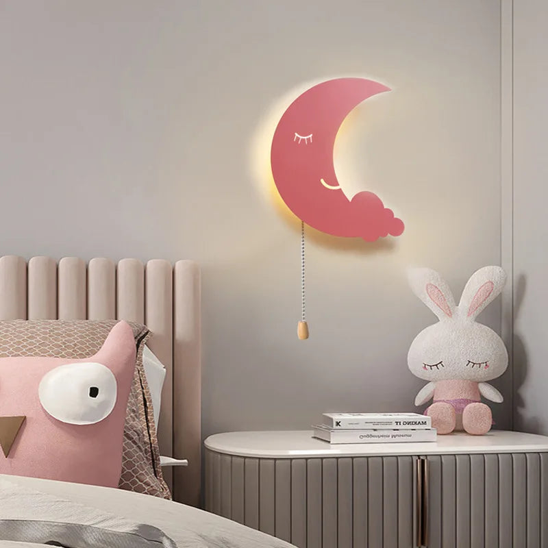 Pink moon wall lamp with sleeping face and hanging pull cord mounted above bed