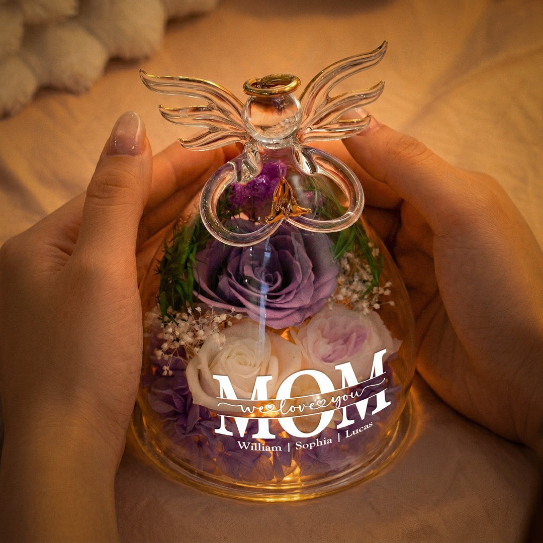 Hands holding a purple preserved rose glass angel figurine glowing warmly in a cozy setting