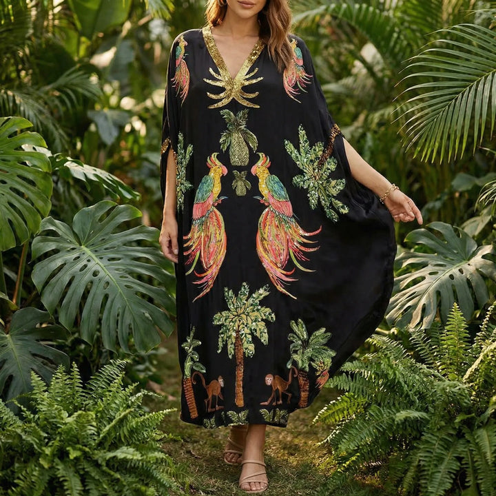 Model wearing black tropical print kaftan dress outdoors among lush greenery