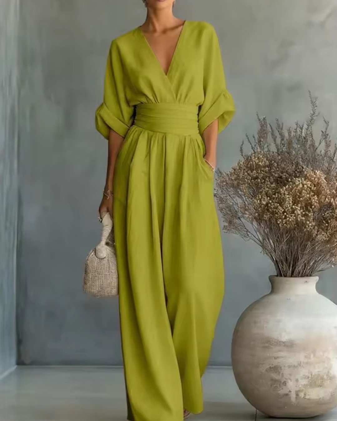 Woman wearing the green V-neck long sleeve jumpsuit holding a woven bag