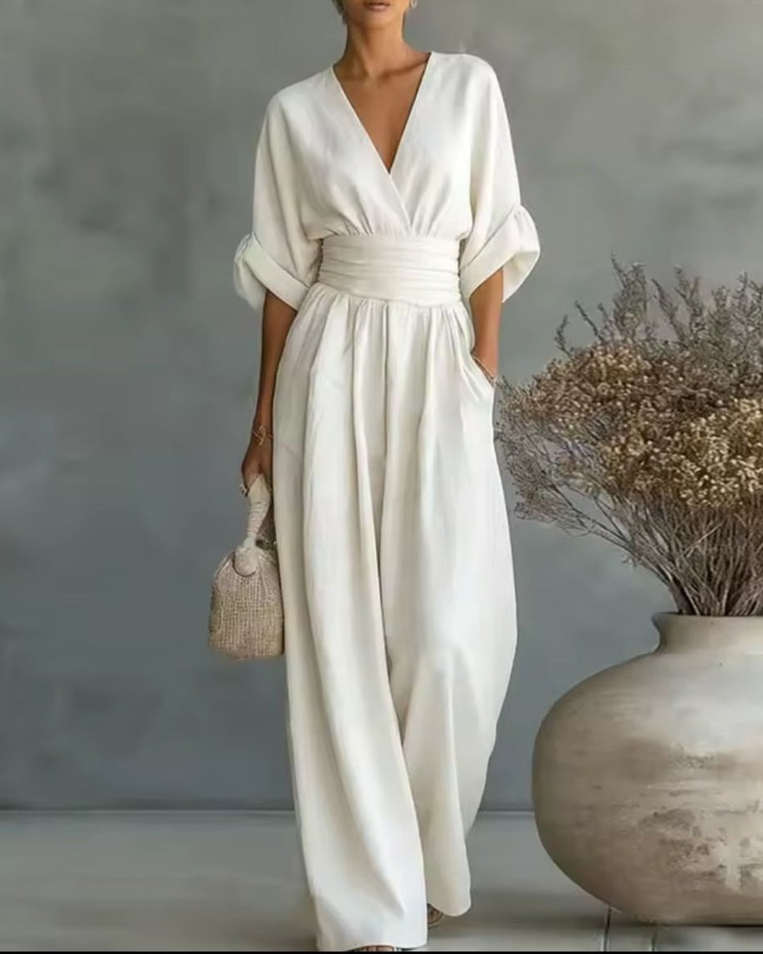 Woman wearing the white V-neck long sleeve jumpsuit holding a woven bag
