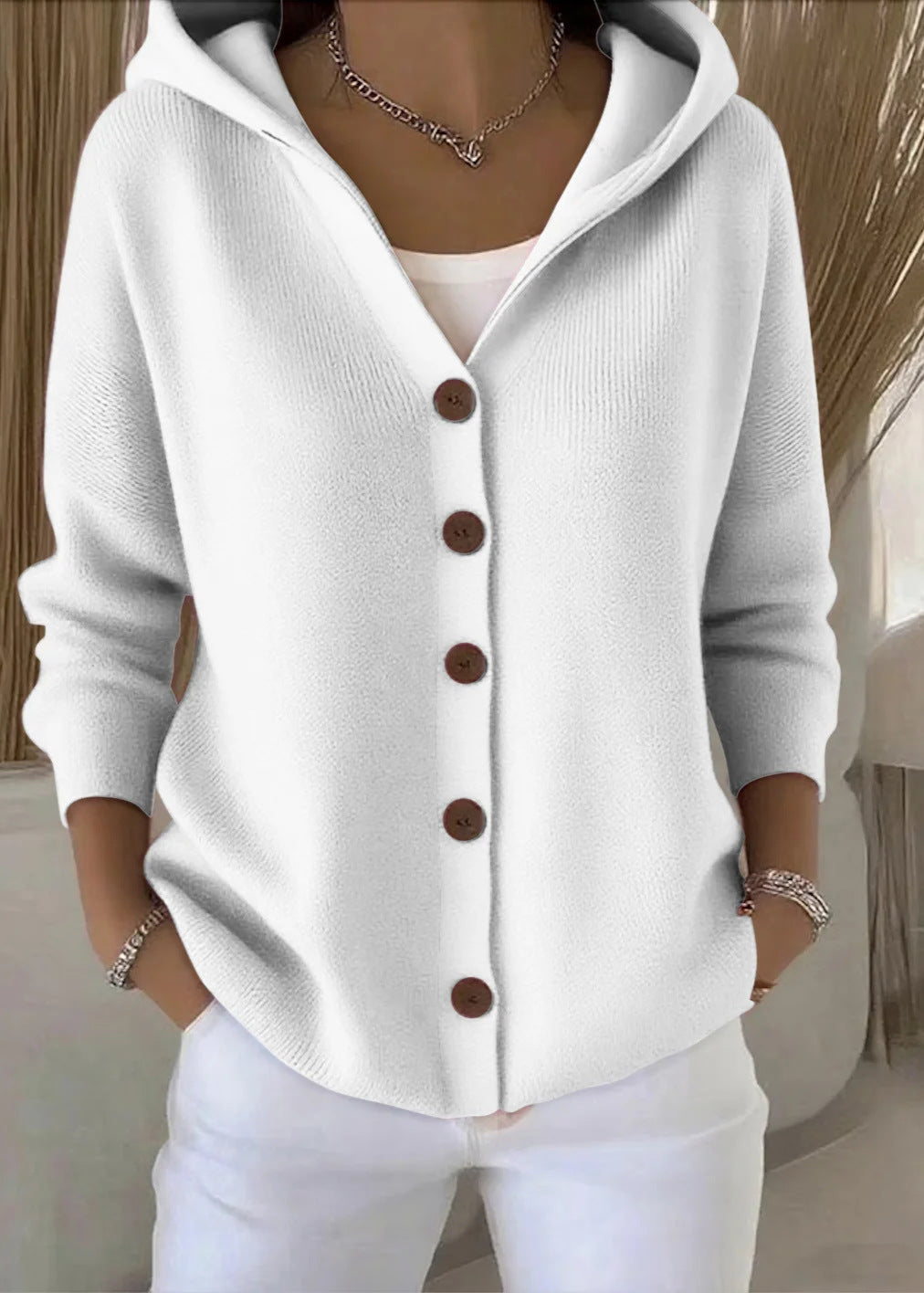 Woman wearing a white hooded button knit cardigan paired with white trousers.
