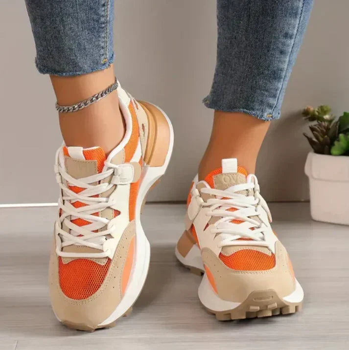 Close-up of women's orange, beige, and white colour-block trainers worn with blue jeans