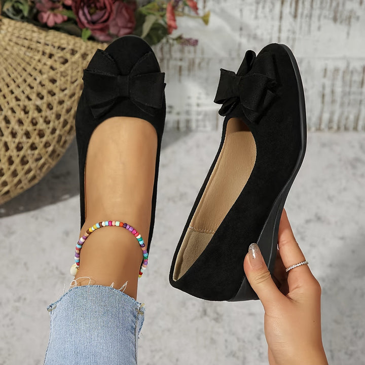 Black women's orthopedic wedge ballet flat with bow detail held in hand